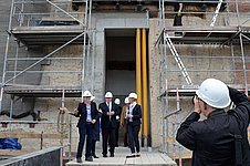 Mehrere Menschen mit weißen Bauhelmen werden von einem Mann mit weißen Bauhelm auf einer Baustelle fotografiert