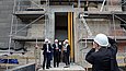 Mehrere Menschen mit weißen Bauhelmen werden von einem Mann mit weißen Bauhelm auf einer Baustelle fotografiert