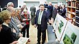 Ein Mann erklärt einer Gruppe etwas, er zeigt auf eine Reihe von Aquarellen mit Parkmotiven