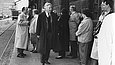 Schwarz-weiß-Foto eines Mannes mit Trenchcoat inmitten einer Menschengruppe an einem Bahnsteig