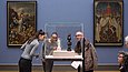 In einem Ausstellungsraum sehen mehrere Menschen sich Objekte in einer Glasvitrine an