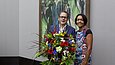 Ein Mann und eine Frau posieren mit einem großen Blumenstrauß vor einem Gemälde