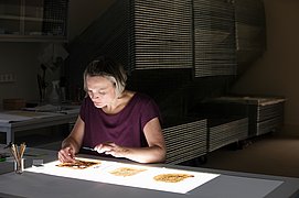 Marie Grotewohl bearbeitet eine beschädigte Handschrift auf einem beleuchteten Arbeitstisch.
