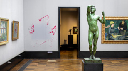 Ausstellungsraum mit Skulpturen und Gemälden, an einer Wand rote Farbspritzer