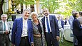 Zwei Männer und eine Frau posieren vor der Festgesellschaft