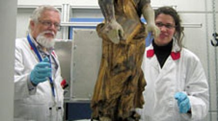 Two people in lab coats looking at a stone sculpture being examined with an instrument