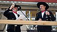 Zwei Männer in klassischer Zimmermannskluft stehen auf einem Baugerüst und halten jeweils ein Glas Sekt in die Höhe