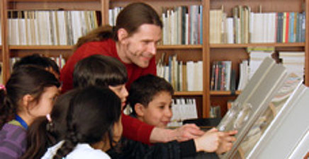 Mann zeigt mehreren Kindern Abbildungen in einem Buch