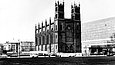 Schwarz-Weiß-Foto einer sanierungsbedürftigen neogotischen Backsteinkirche neben einem modernen Glas-Stahl-Bau