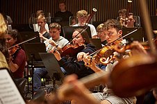 Musiker*innen des Bundesjugendorchesters spielen gemeinsam auf einer Konzertbühne.
