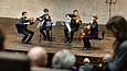 Vier Personen spielen auf einer Bühne vor Publikum Musikinstrumente
