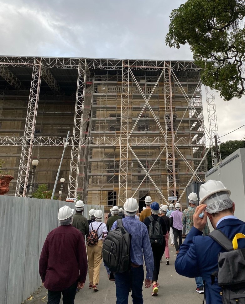 Several people with white hard hats approach a scaffolded building