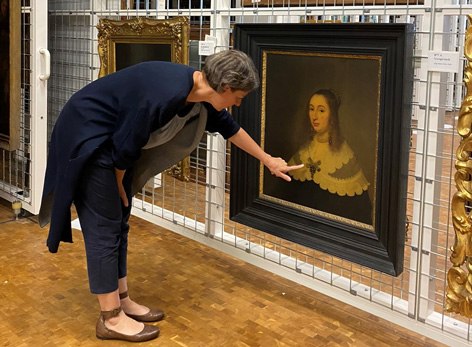 A woman looks at a painting in a storage room