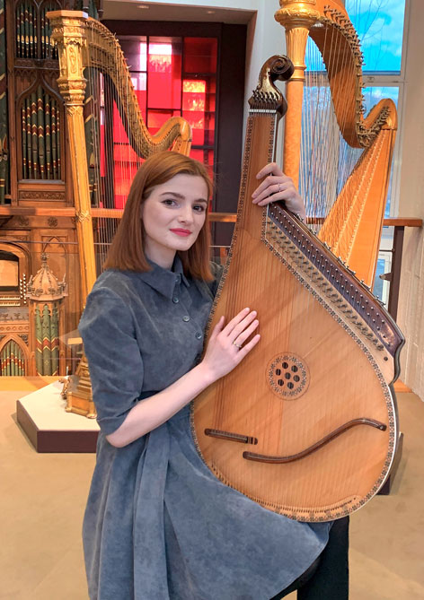 A seated woman holds a large stringed instrument in her hand