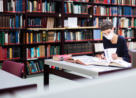 Using the library of the IAI only with a mask Woman in a library wearing a mask