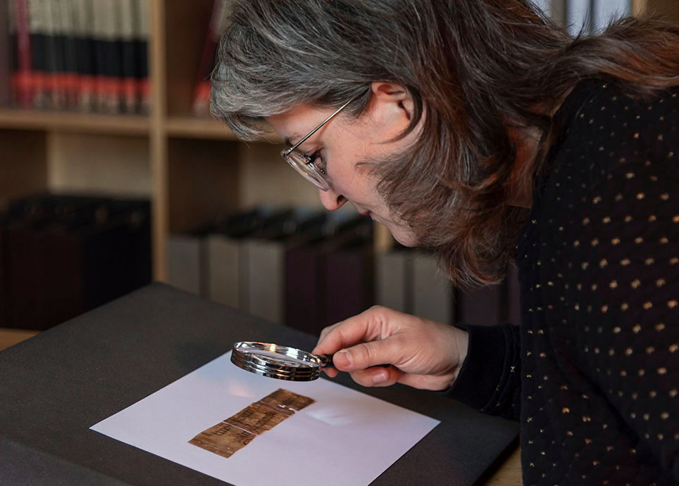 A woman looks at a historical document through a magnifying glass