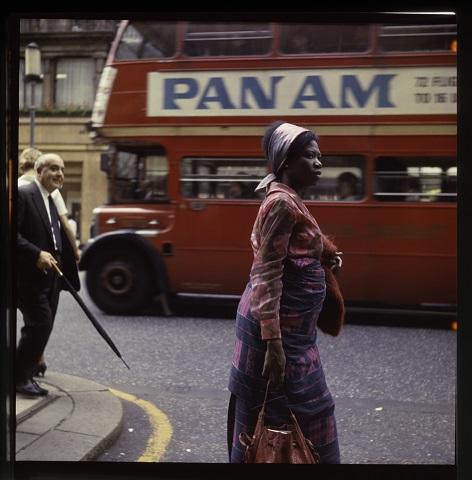 Straßenszene in London Eine Frau geht über die Straße, hinter ihr ein roter Doppeldeckerbus mit der Werbeaufschrift "Pan Am"