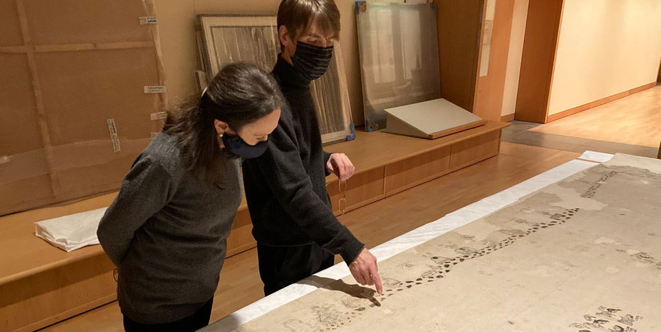 Two people view a historical cotton cloth laying flat on a large table