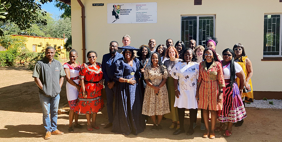 Eröffnung des Museum of Namibian Fashion in Otjiwarongo © SPK / Stefan Müchler Eine Gruppe von rund dutzend Menschen bei Sonnenschein auf Lehmboden vor einem hellgelb getünchten Haus stehend