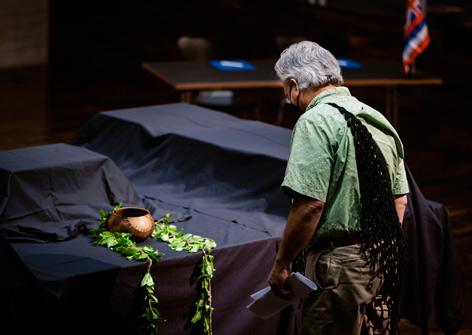 Edward Halealoha Ayau with the iwi kūpuna A man stands upright in front of them with a black cloth covered table