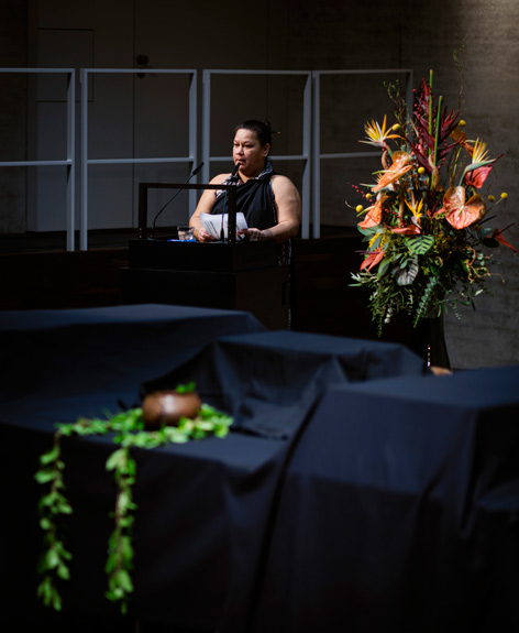 A woman speaks at the ceremony, there is a table covered with black cloth