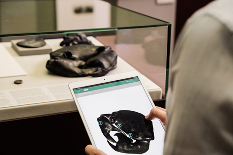 Münzkabinett Eine Person hält ein Tablet in der Hand und steht vor einer flachen Glasvitrine