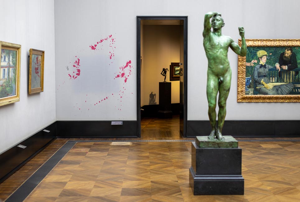 Ausstellungsraum mit Skulpturen und Gemälden, an einer Wand rote Farbspritzer