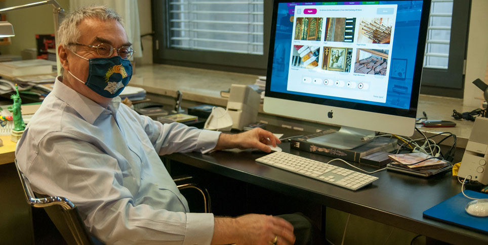 Ein Mann mit Mundschutz sitzt an einem Bildschirm in einem Büro.