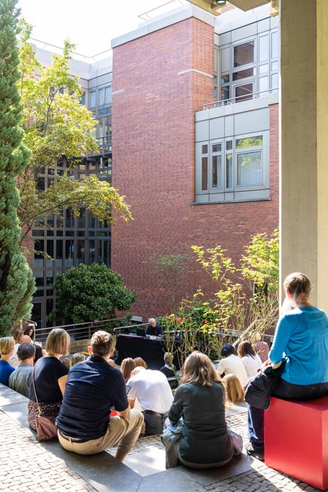 Arnold Dreyblatt bringt im anderen Innenhof des Kunstgewerbemuseums den softbrutalistischen Bau zum Klingen © Stefanie Heider Ein Mann bedient im Innenhof eines Backsteinbaus einen Synthesizer, Menschen sitzen drum herum und lauschen