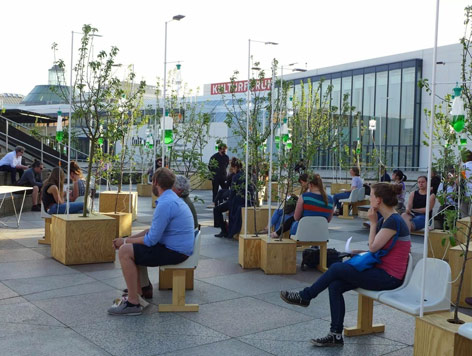 Performance zur Ausstellung „Food Revolution 5.0“ Menschen sitzen auf einem Platz mit Bäumen