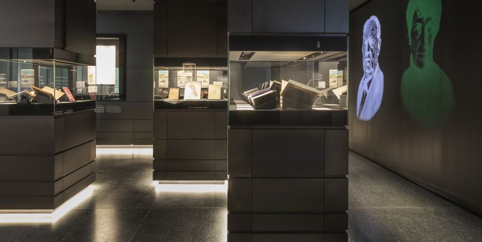 Kulturwerk Blick in eine dunkle Ausstellung mit beleuchteten Vitrinen