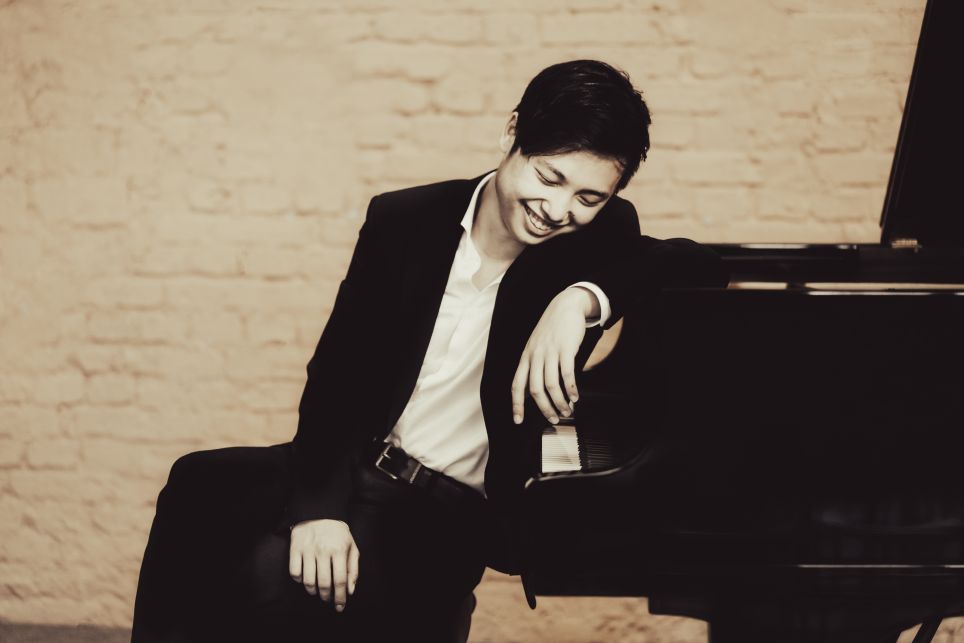 Der Pianist Jeonghwan Kim sitzt lachend an einem Konzertflügel. (c) Jeonghwan Kim