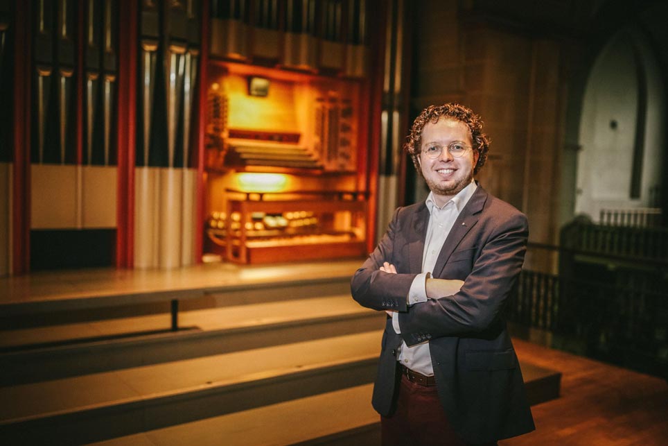 Sebastian Küchler-Blessing, ein Mann mit Brille, steht vor einer Orgel.