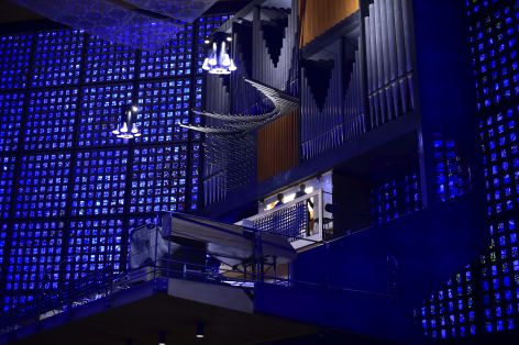 Ein Kirchenraum in blaues Licht getaucht, an einer großen Orgel sitzt eine Person und spielt.