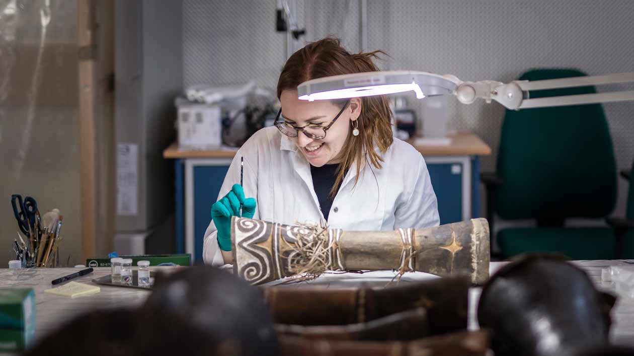 In der Restaurierungsstraße in Dahlem werden die insgesamt rund 10.000 Objekte für den Umzug ins Humboldt Forum vorbereitet. Eine Restauratorin arbeitet mit einem feinen Instrument an einem Holzobjekt