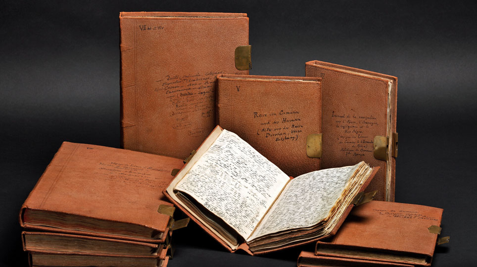 Neun alte Buchbände, eines davon aufgeschlagen mit handschriftlich beschriebenen Seiten