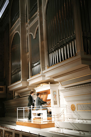 Ein Mann spielt Orgel, während ihm ein anderer Mann über die Schulter blickt (öffnet Vergrößerung des Bildes)