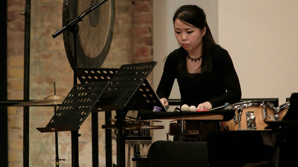Eine Frau steht zwischen Musikinstrumenten und Notenständern (öffnet Vergrößerung des Bildes)