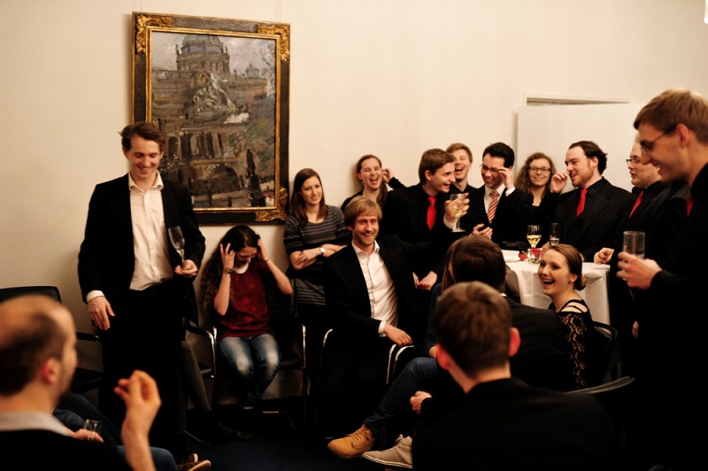 Mehrere Menschen sitzen und stehen verteilt in einem Raum (öffnet Vergrößerung des Bildes)