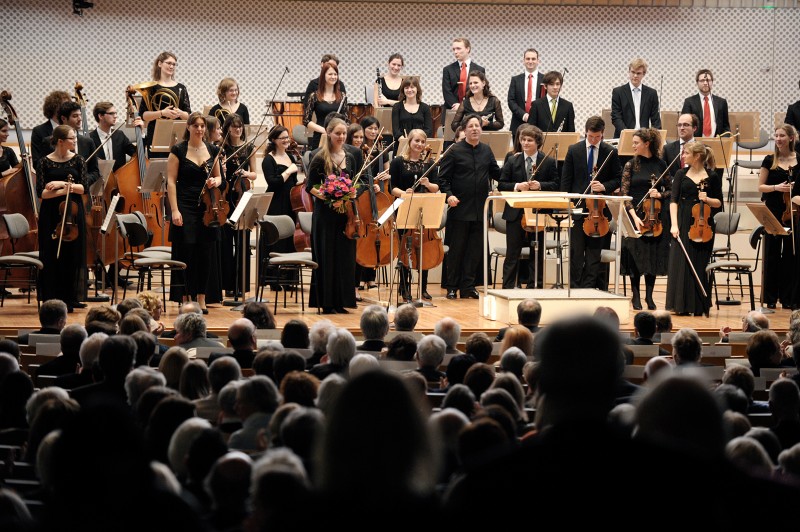Ein Orchester steht vor einem Publikum auf der Bühne (öffnet Vergrößerung des Bildes)