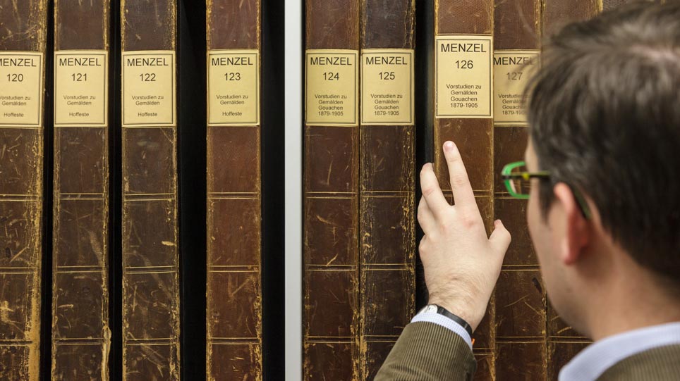 Man takes a file of drawings by Adolph Menzel from a shelf (opens enlarged image)