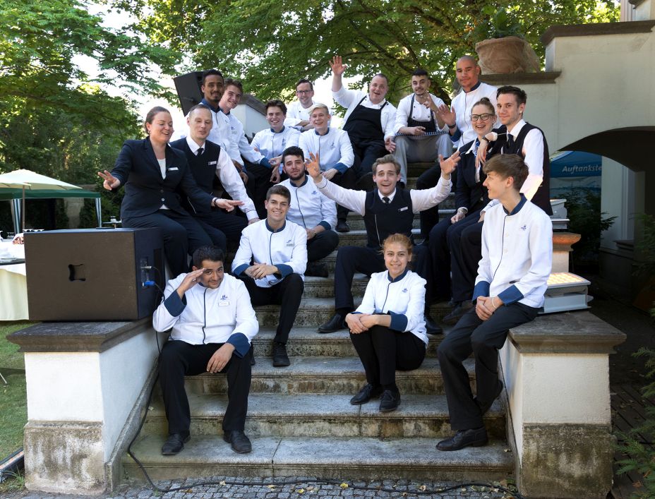 Das Team von Maritim freut sich auf die Gäste des Gartenempfangs 2018 Mehrere junge Menschen sitzen auf einer Treppe im Freien