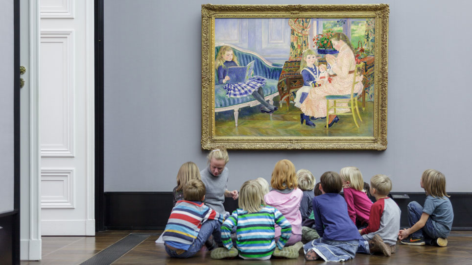 A woman and a group of children sit on the floor in front of a painting