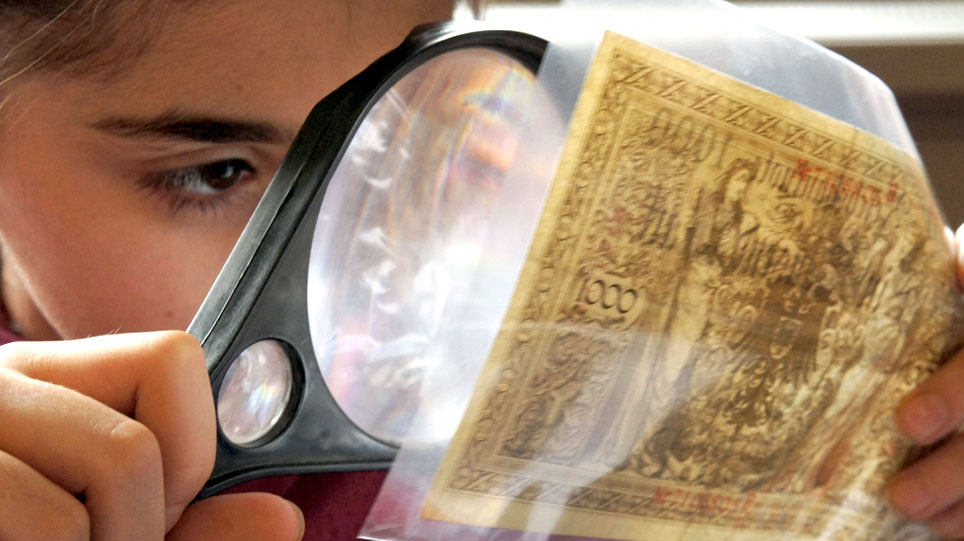 A child examines a bank note through a magnifying glass