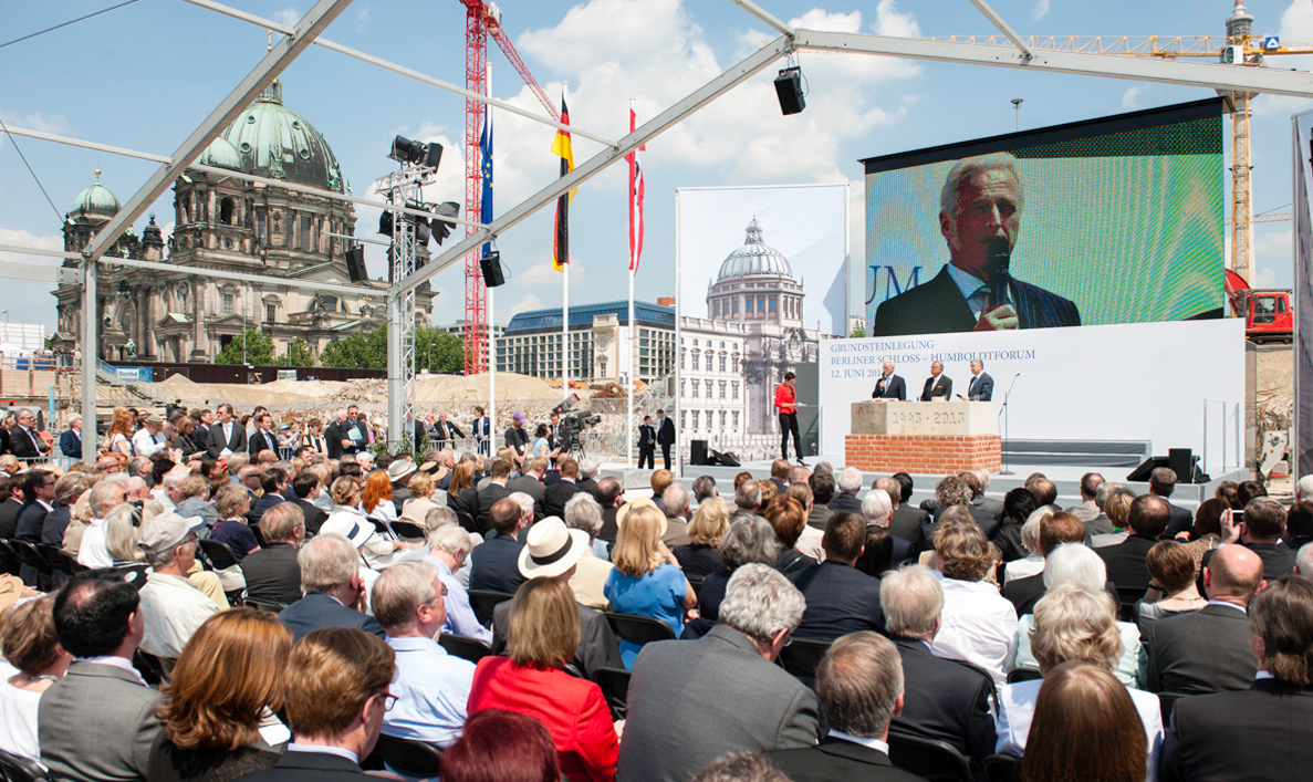Drei Männer sprechen unter freiem Himmel auf einer Bühne vor Publikum