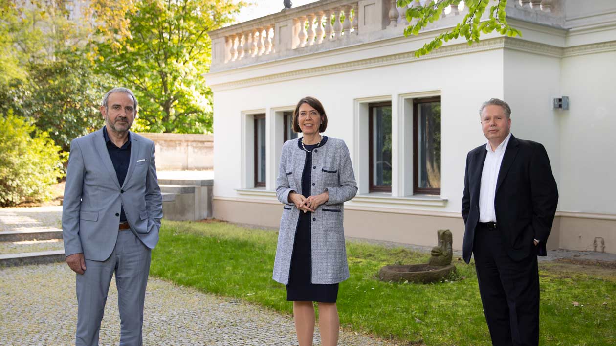 Drei Personen stehen im Garten einer Villa