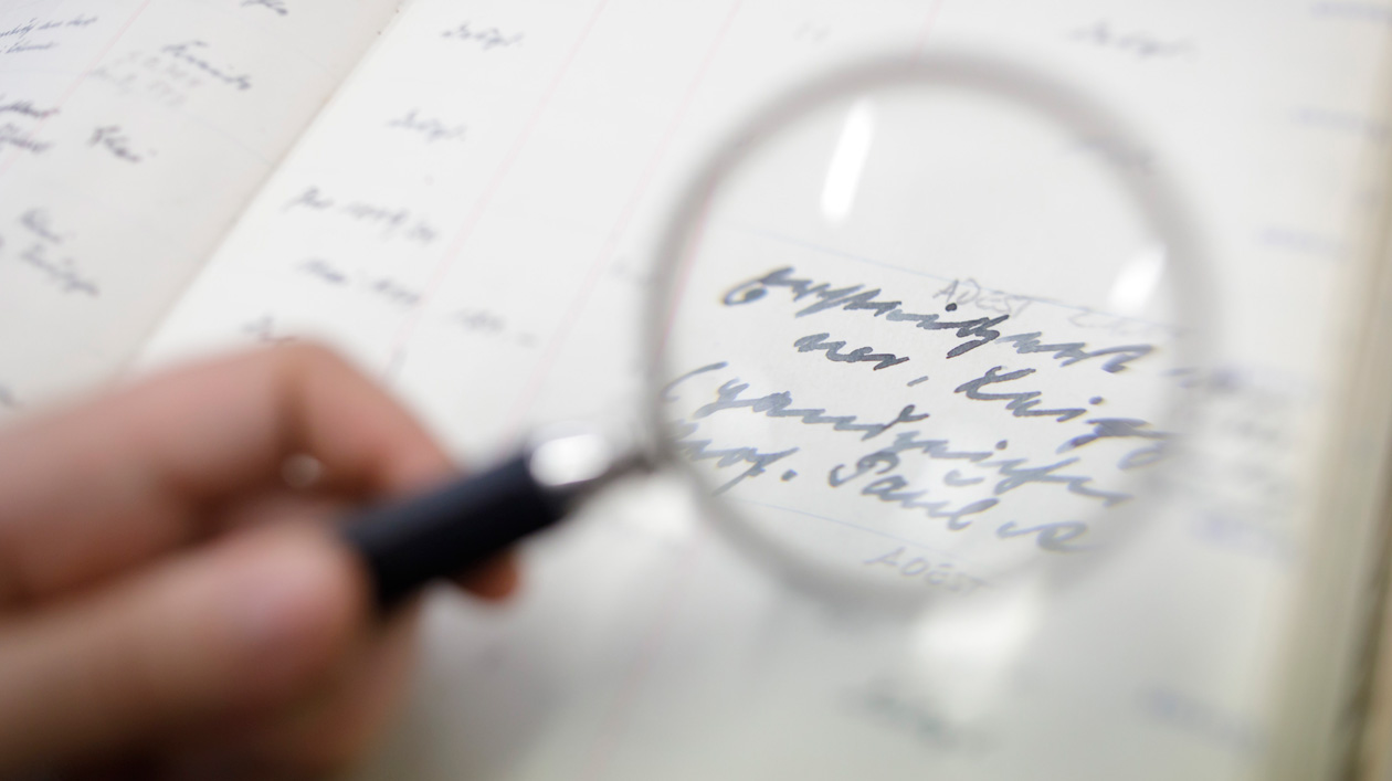 A person holds a magnifying glass over a sheet of paper