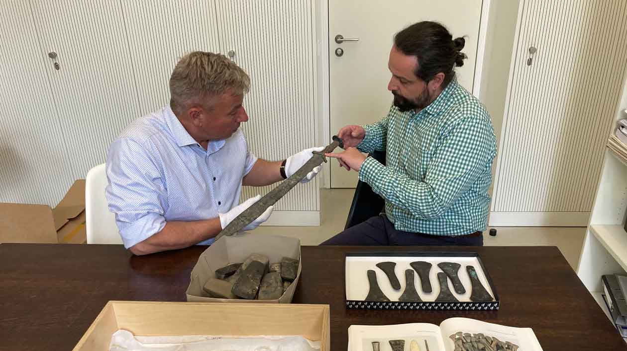 Two men look at a bronze sword