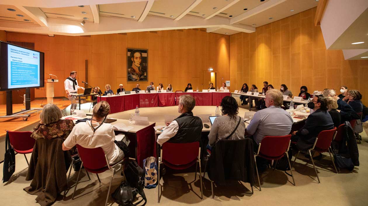 Forschung und Praxis der Wissensproduktion und -Archivierung. Dialog mit Lateinamerika Menschen sitzen in einem Sitzungssaal im Halbkreis, ein Mann spricht vor einer Präsentation