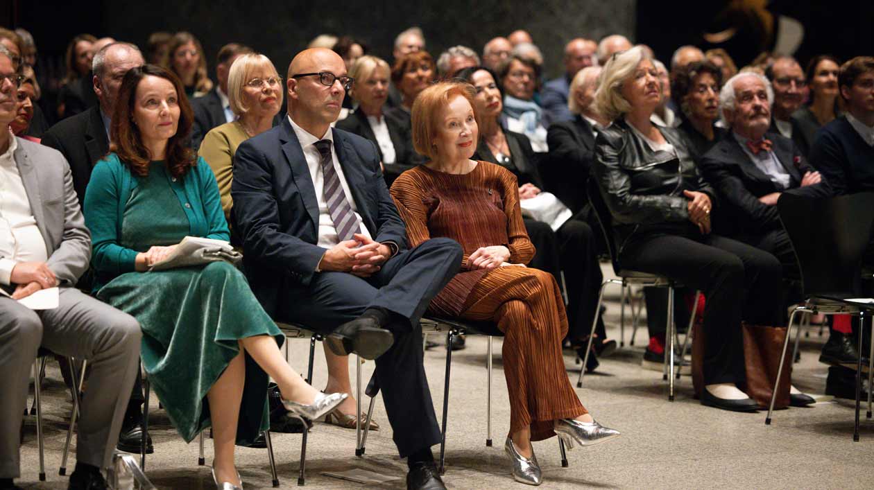 Several people are seated on chairs in a moody, modern exhibition hall